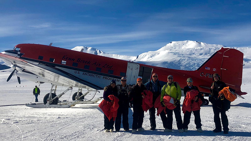 The team poses for a photo in front of the airplane that brought them to Shackleton field camp. (Left to right) Melisa Diaz, Mountaineer Geoff Schellens, Diana Wall, Noah Fierer, Byron Adams, Marcella Adams and Ian Hogg
