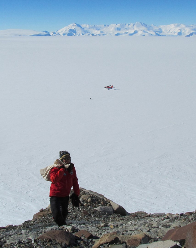 With the Twin Otter plane in the background, Erik Gulbranson carries a bag full of ash samples