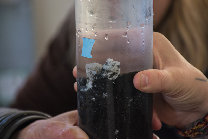Inside a sample vial, a small portion of the white, sulfide-laced microbial mats is preserved