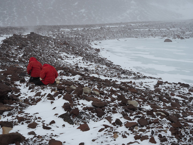 Jen Lamp and Kate Swanger collect rock samples along the headwall of the Mullins Glacier in inclement weather.