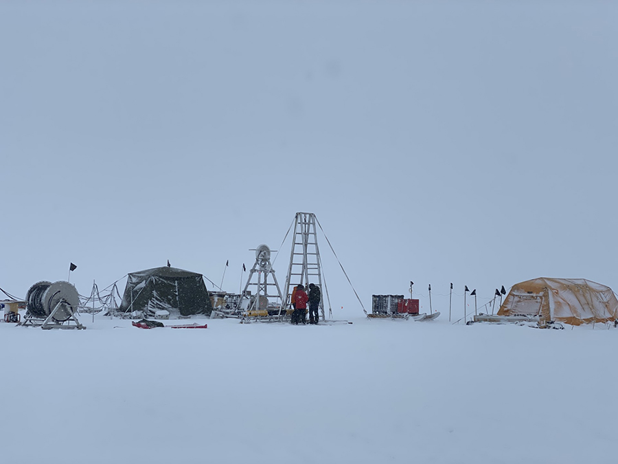 The field camp at Cavity Camp under cloudy skies with the drilling rig visible in the center along with the robot control tent on the right. 