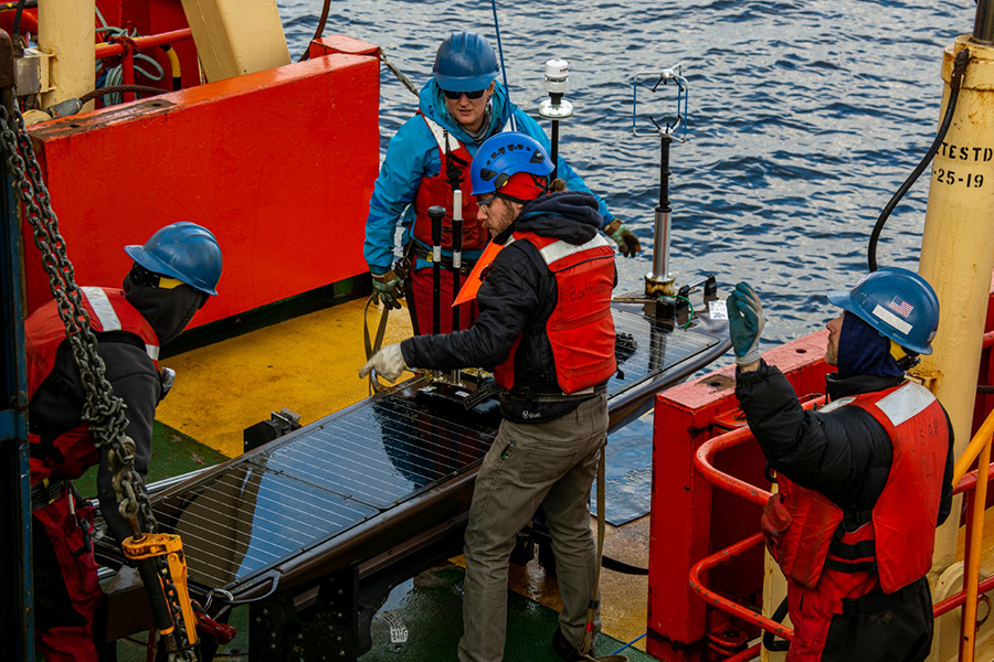 After hoisting the Wave Glider ASV up to the deck, Ryan Newell (center) and marine technicians on board the research vessel Laurence M. Gould work to secure it and pack it for transport back home.