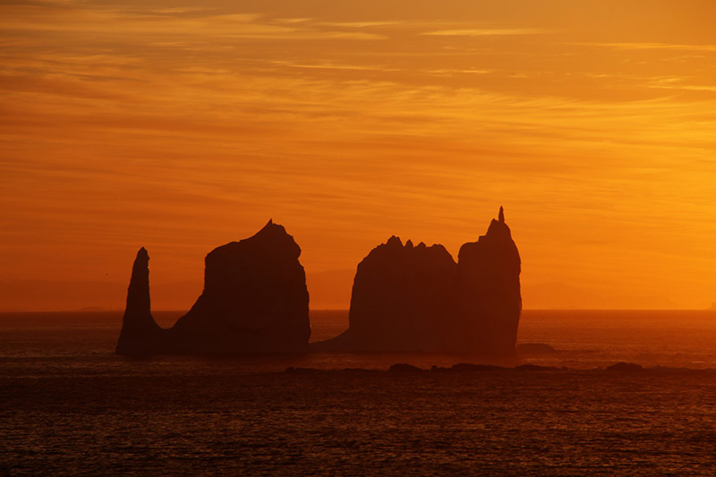 The sun sets on Palmer Station, silhouetting the pinnacles of a passing iceberg