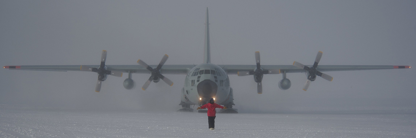 A worker at the South Pole marshals a taxiing LC-130 Hercules