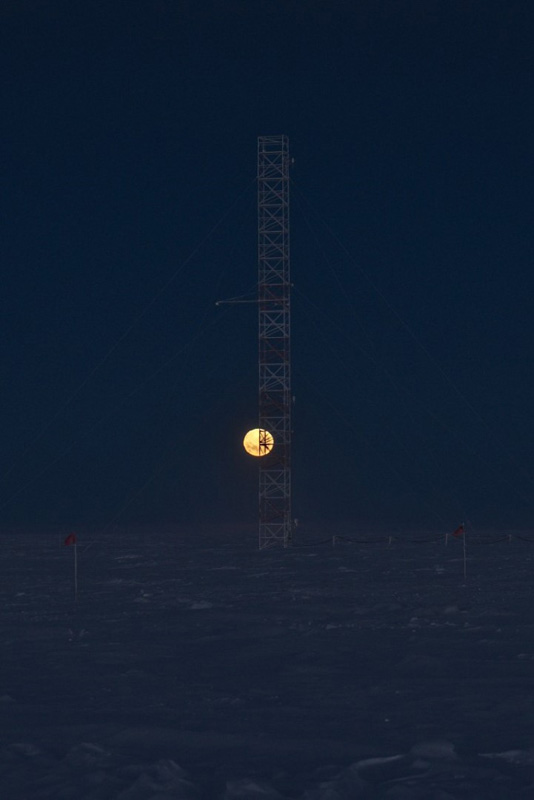 Behind a scaffolding tower, a full moon rises over the horizon