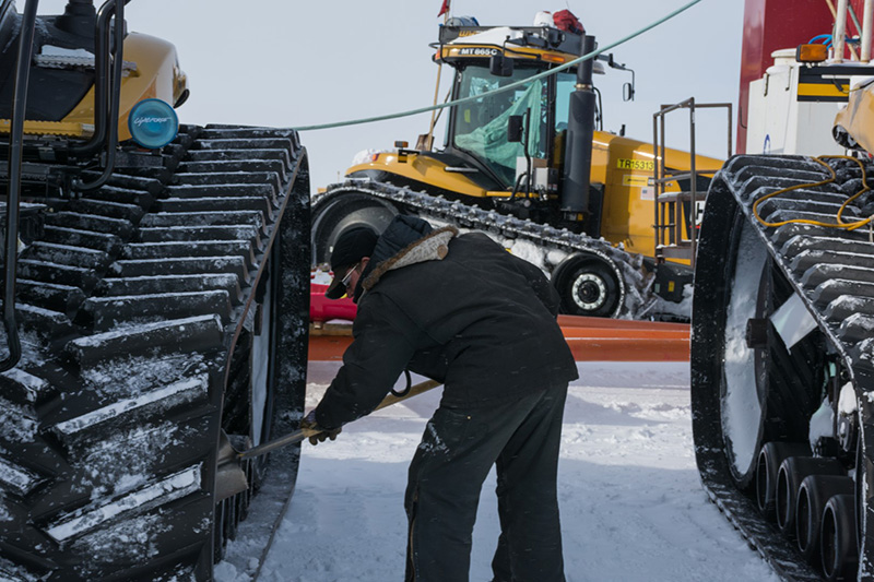 After arriving at the South Pole, Stephen Kriete knocks snow off of his tractor. After staying for a few days at the station, the SPoT Team will climb back into their tractors and drive back to McMurdo.