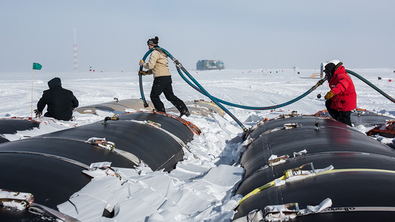 (Left to right) Jarred (Red) Taylor, Ben Eberhardt and Tim Mullen haul a hose over recently-delivered fuel bladders at the South Pole. They're brought by the South Pole Traverse, a fleet of tractors that hauls them over 1,000 miles from McMurdo Station.
