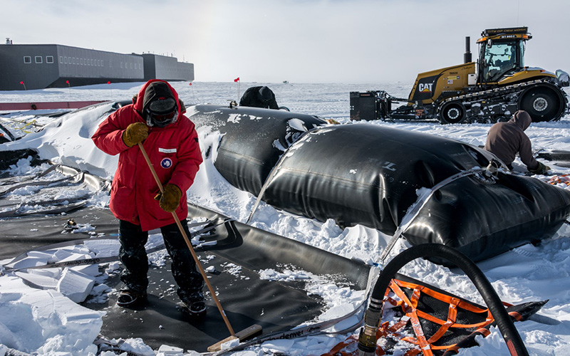 Tim Mullen sweeps the last few drops out of the fuel bladder. In the background sits one of the tractors that hauled the fuel from McMurdo Station 1,000 miles away. Mullen was one of the tractor drivers for the fleet.