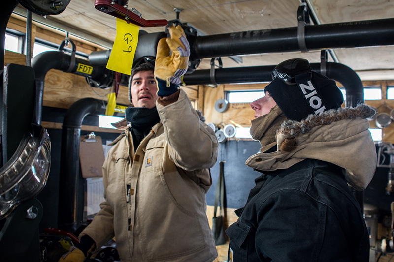 South Pole fuels foreman Jarred (Red) Taylor (right) shows Ben Eberhardt how the fuel pumping station works.