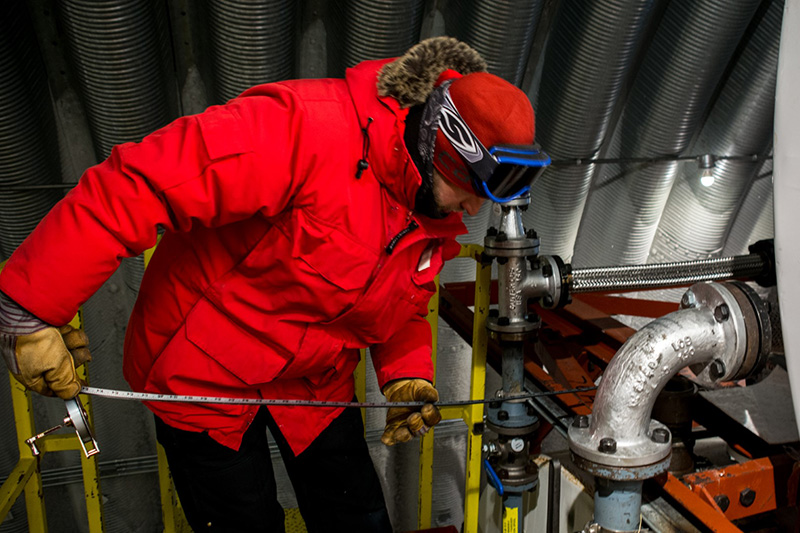 In the Fuel Arch, below the surface of the South Pole, fuels supervisor Chad Goodale dips a tape measure into one of the storage tanks to see how full it is.