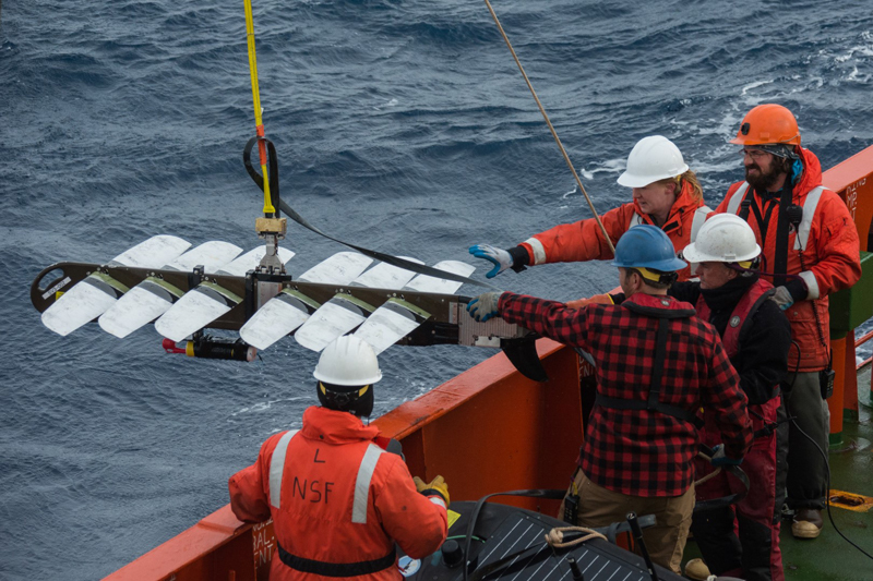 (Left to right) Sean Bercaw, Dave Moore, Amy Belcher, Chuck Holloway and Matt Lewis help to pull a wave gliders propulsion system out of the ocean after recovering it in the Drake Passage