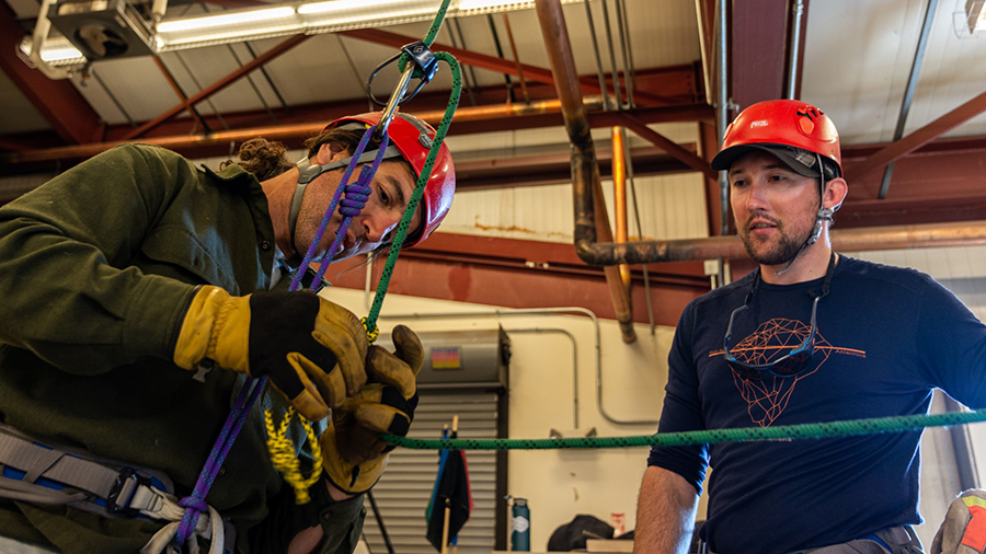 In a classroom environment, field safety coordinator Mitch Beres (right) helps train Federico Piola on how to correctly wear his climbing harness.