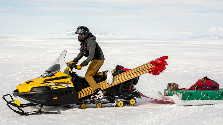 Riding a snowmobile with a load of flags, Mitch Beres drives along one of the ice roads around McMurdo Station making sure the safe routes are clearly marked.