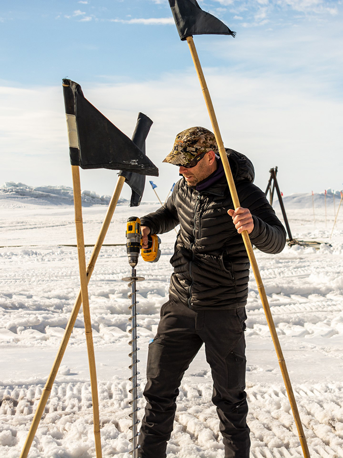 Using a drill to punch a hole in the frozen ground, Philippe Wheelock sets up black flags, marking a hazard by one of the station's ice roads.